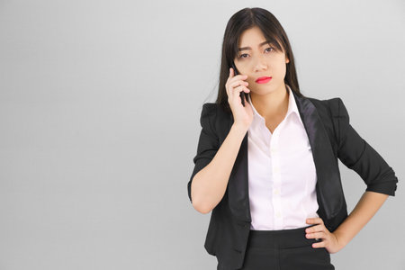 Young Asian women in suit standing posing using her phone against gray backgroundの写真素材
