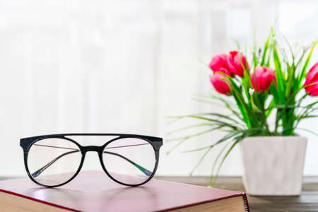 Reading glasses put on hardcover books over wooden table beside the windowの写真素材