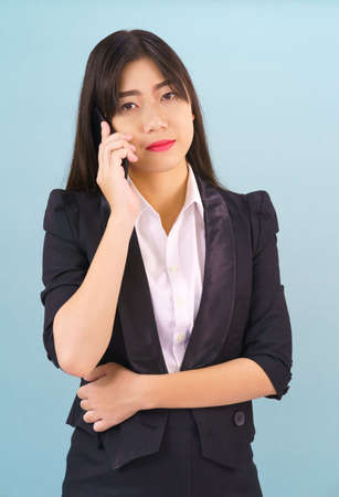 Young Asian woman in suit standing posing using her phone against blue backgroundの写真素材