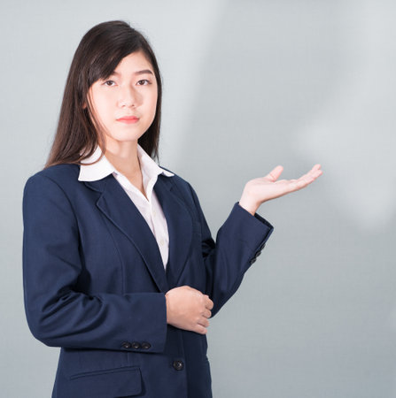Asian woman in suit open hand palm gestures with empty space on gray backgroundの写真素材