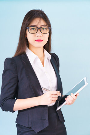 Young Asain woman in suit standing using her digital tablet against blue backgroundの写真素材