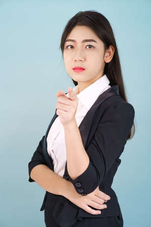 Asian woman looking at camera and pointing finger on blue backgroundの写真素材