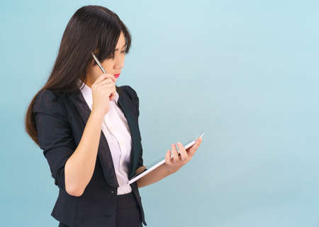 Young Asain women in suit standing using her digital tablet against blue backgroundの写真素材