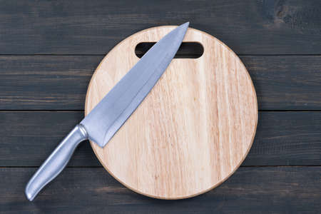 Close up kitchen knife and wooden round empty cutting board on a wooden tableの写真素材