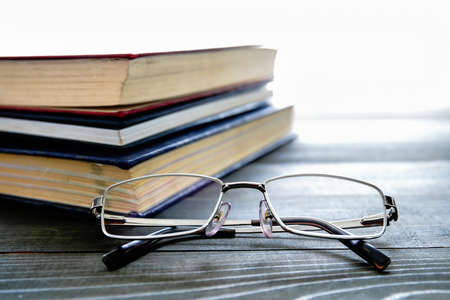 Glasses and stack of hardcover books over wooden tableの写真素材