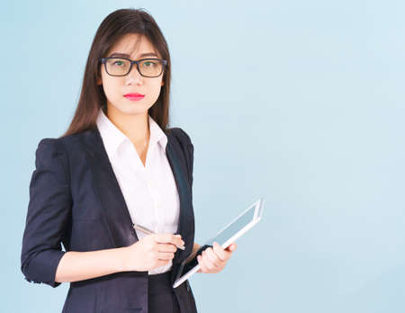 Young Asain women in suit standing using her digital tablet against blue backgroundの写真素材