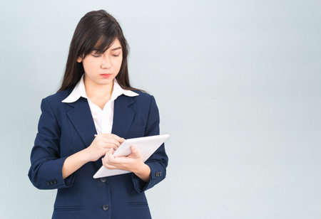 Asian woman in suit using computer digital tablet isolated on gray backgroundの写真素材