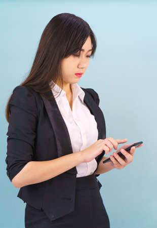 Young Asian women in suit standing posing using her phone against blue backgroundの写真素材