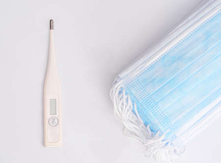 Medical respiratory surgical face mask filter with digital clinical thermometer ,Close-up of surgical medical mask on whiteの写真素材