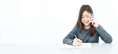 Close up woman long hair writing notebook and using mobile phone on white backgroundの写真素材