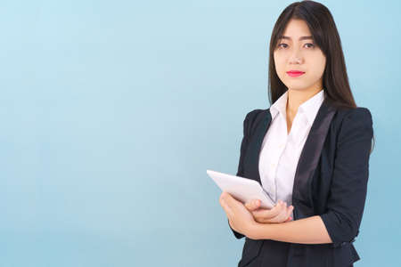 Young women standing in suit holding her digital tablet computor against blue backgroundの写真素材