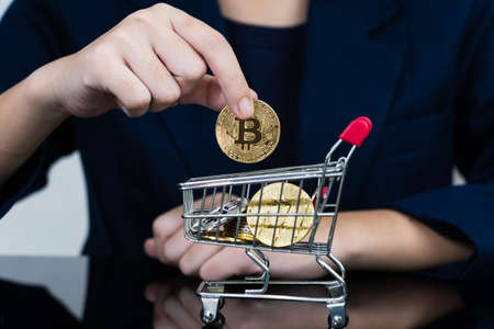 Close up of business woman holding some pieces of golden Bitcoin token in shopping cart, Bitcoin is one of the popular cryptocurrencyの写真素材
