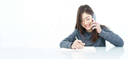 Close up woman long hair writing notebook and using mobile phone on white backgroundの写真素材