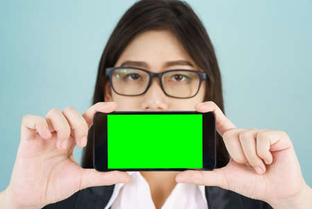 Young women in suit holding her  smartphone mock up green screen standing against blue backgroundの写真素材
