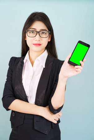 Young women in suit holding her  smartphone mock up green screen standing against blue backgroundの写真素材