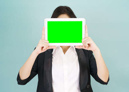 Young asian women in suit holding her digital tablet mock up standing against green backgroundの写真素材