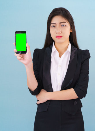 Young women in suit holding her green screen smartphone mock up standing against blue backgroundの写真素材