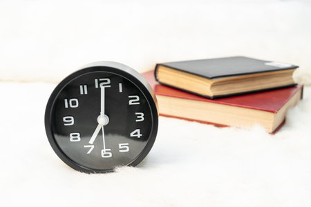 Close up Black alarm clock and book stacked on tableの写真素材