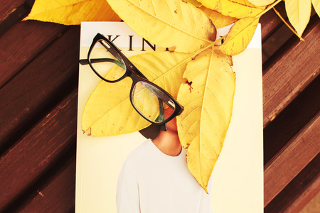 glasses with a magazine on a bench in autumn parkの写真素材