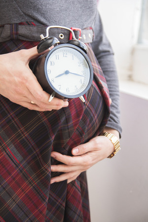 Pregnant woman holding a clock at the stomachの写真素材