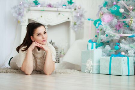girl lying near a white Christmas tree with giftsの写真素材