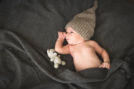 newborn baby with a toy lying next to the knitted teddy bearの写真素材