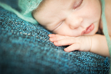 newborn baby sleeping sweetly on a blue rug in blue capの写真素材