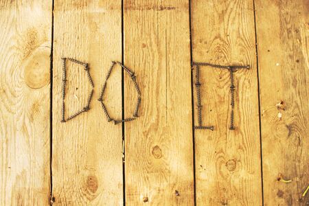 the inscription Do It on the wooden background of screws