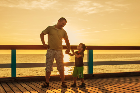 Dad and son playing at the pier on the sea at sunsetの写真素材