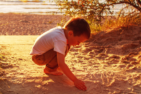 boy playing with sand on the beach. sunsetの写真素材