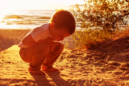 boy playing with sand on the beach. sunsetの写真素材