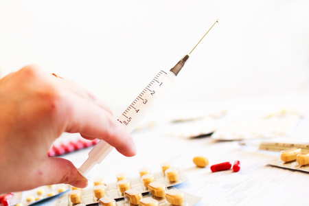 Syringe with medicine in the hand and a lot of tablets on the tableの写真素材