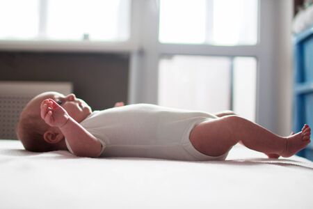 the infant lies on the bed in front of the window