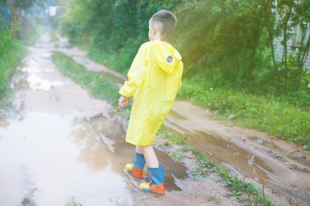 child in rubber boots playing in a puddle