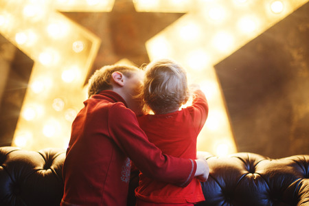 brother hugs sister back. children hugging in the background of lightsの写真素材