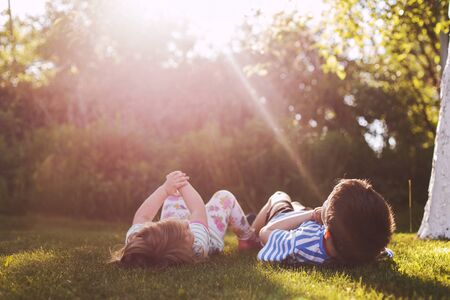 brother with  his little sister outdoor back. two children lying on the grass in the gardenの写真素材