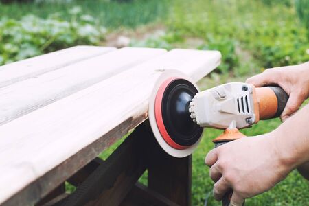 man polishes the board on the bench. man repairing bench in the garden