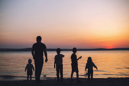people at sunset throwing stones into the water. dad with childrenの写真素材
