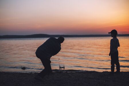 people at sunset throwing stones into the water. dad with son