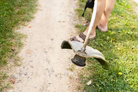 a man mows grass with a trimmer outdoor