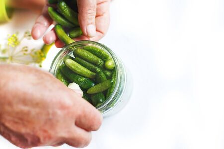 pickled cucumbers in a glass jar. gherkins cucumbers. woman pickles cucumbers on a white backgroundの写真素材