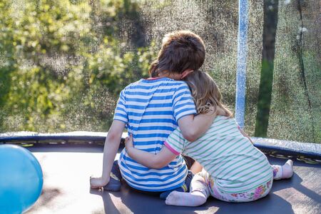 children hugging in the garden on trampoline. brother with  his little sister outdoor backの写真素材