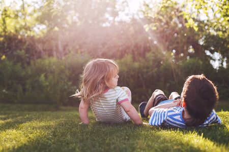 brother with  his little sister outdoor back. two children lying on the grass in the gardenの写真素材