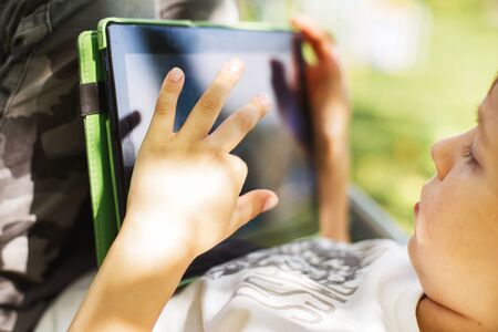 boy sitting with a tablet in the garden. the boy lies on a deck chair and plays on the tablet. child...