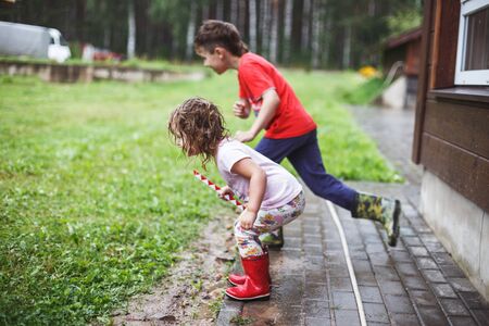 boy and girl play in rainy summer park. Children jump in puddle and mud in the rain. brother and sister play in rainy weather. Outdoor fun by any weather.の写真素材