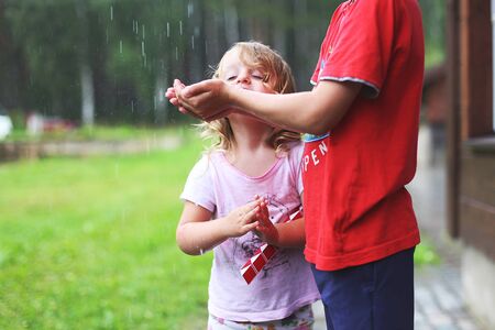 boy and girl play in rainy summer park. Children jump in puddle and mud in the rain. brother and sister play in rainy weather. Outdoor fun by any weather.の写真素材