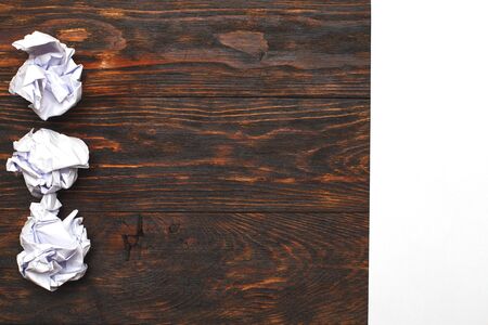 Crumpled up papers with a sheet of blank on brown wooden backgroundの写真素材