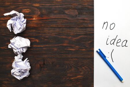 Crumpled up papers with a sheet of blank and a pen on brown wooden backgroundの写真素材