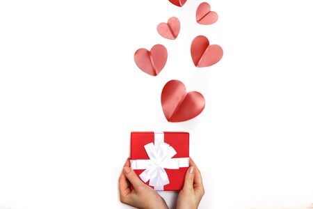 hands of a young woman holding a small present box with red hearts on a white backgroundの写真素材