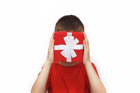 a young man holding a small red present box on a white background. child covers his face with a boxの写真素材